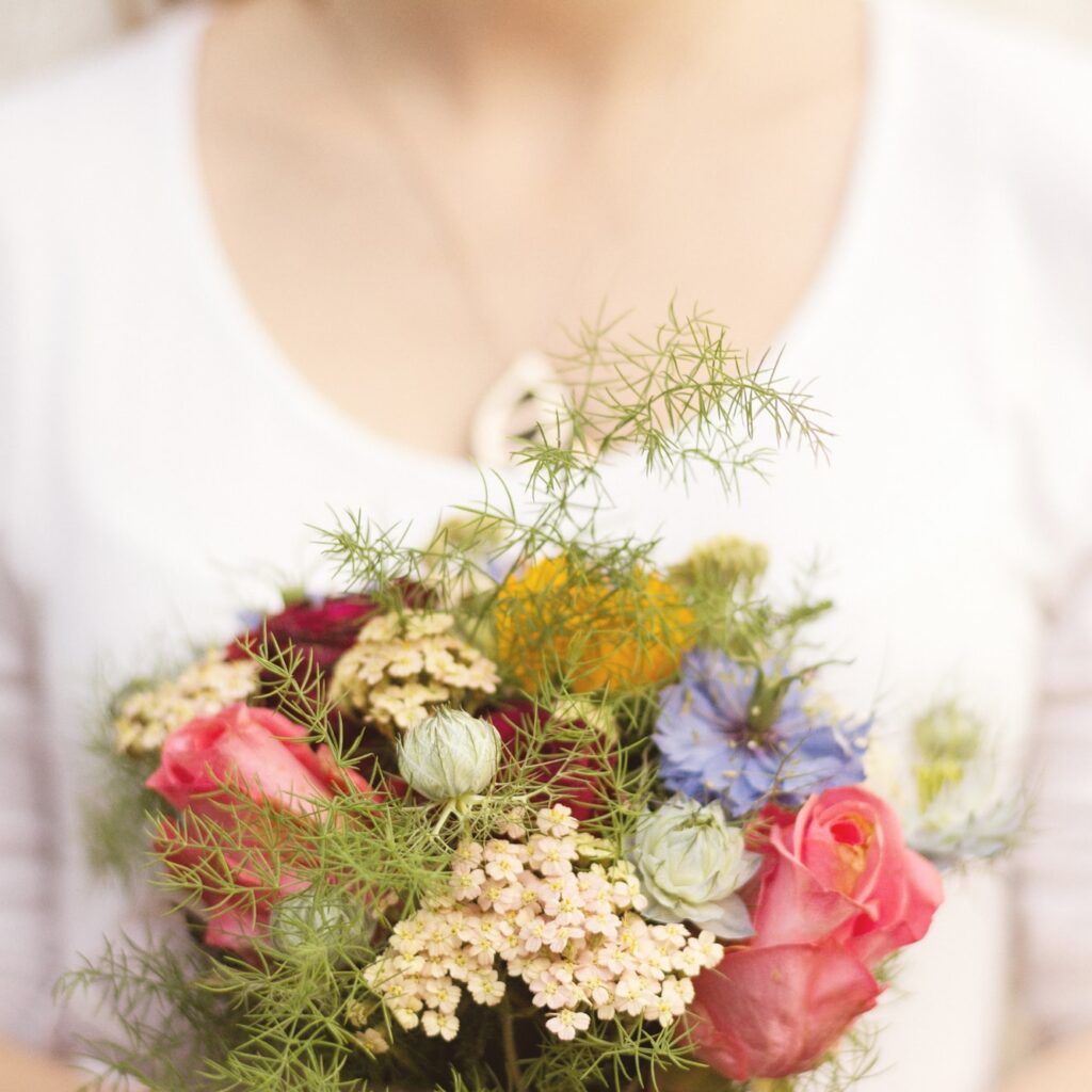 Mulher com blusa branca segurando lindo buque de flores para presente